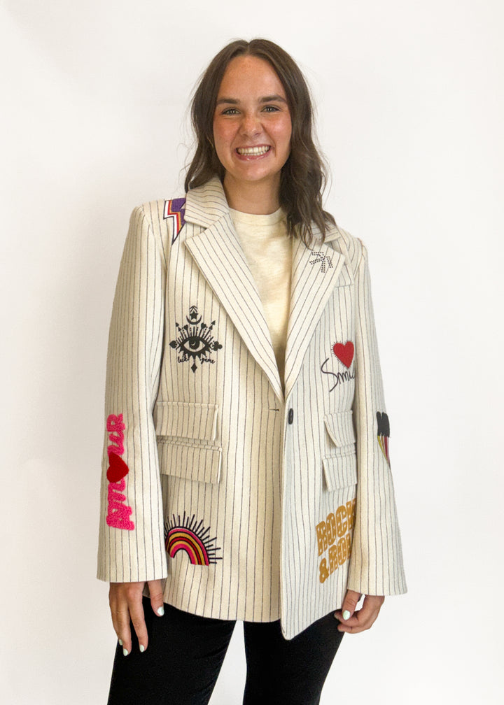 A woman wearing a cream pinstripe blazer with colorful embroidered patches and graphics
