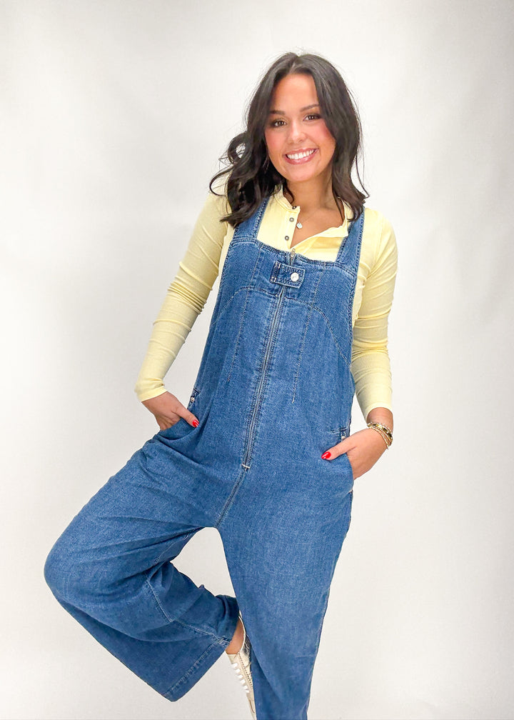 Woman wearing blue denim overalls and a yellow top on a white background