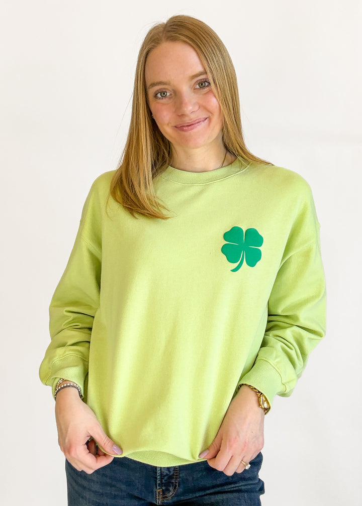 Woman wearing a light green sweatshirt with a four-leaf clover design on a plain background