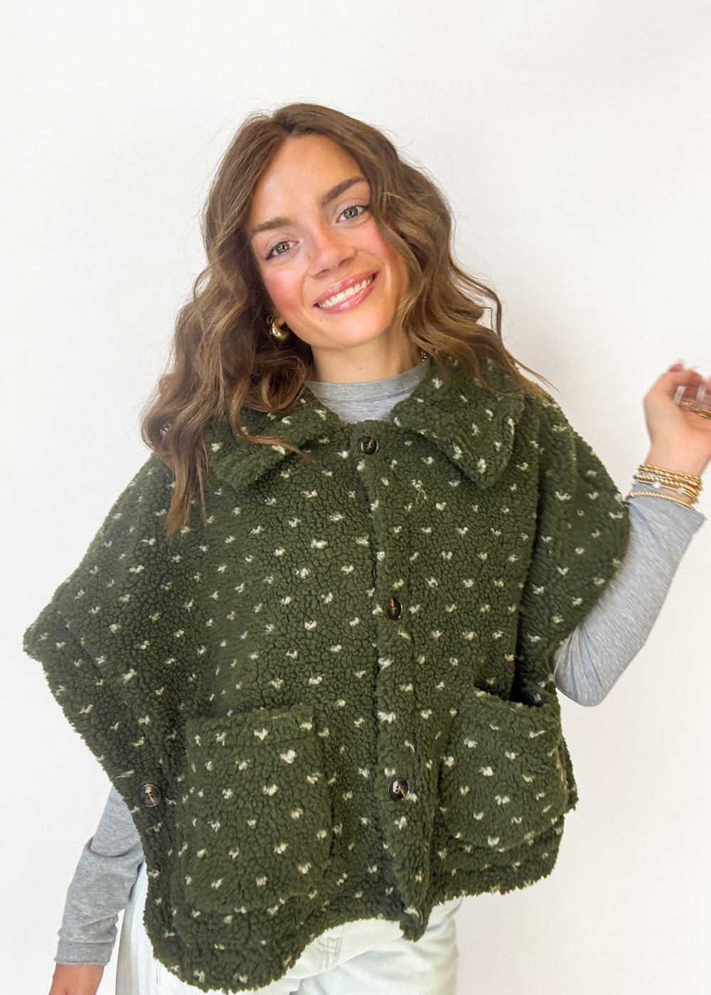 A woman wearing a dark olive green sherpa poncho-style cardigan with a white heart pattern