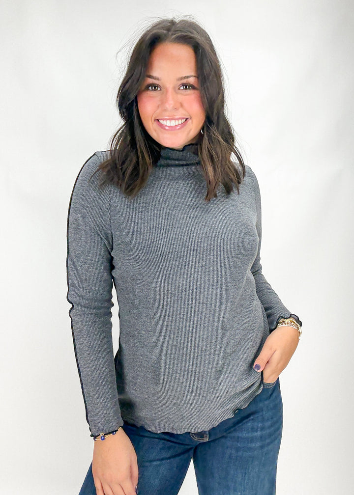 Woman wearing a gray turtleneck sweater and blue jeans on a white background
