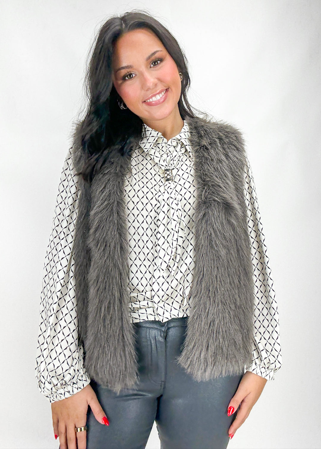 Woman wearing a gray fur vest over a patterned shirt with a white background