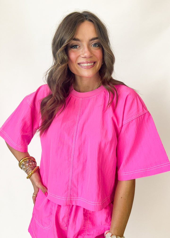 Woman wearing a bright pink cropped top against a plain background