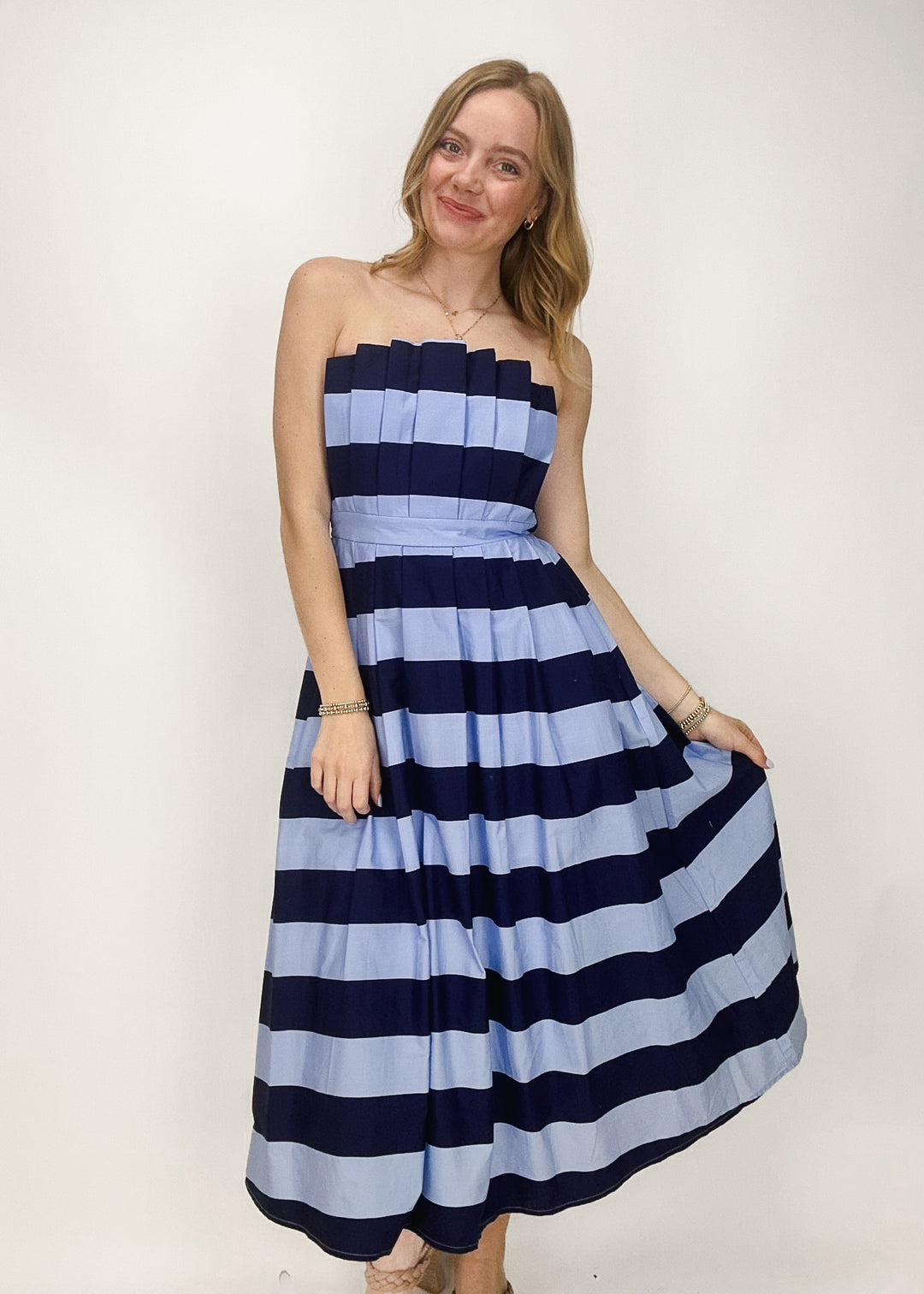 woman wearing two toned blue stripe midi dress with strapless neckline and pleated details
