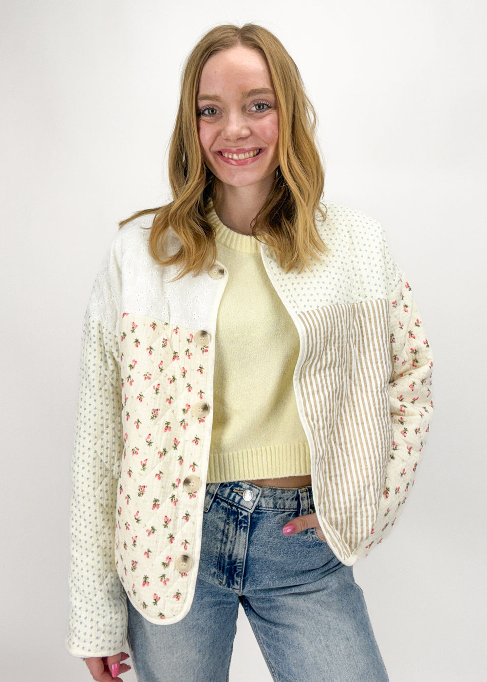 Woman wearing a cream cardigan with floral patterns, yellow sweater, and blue jeans on a white background