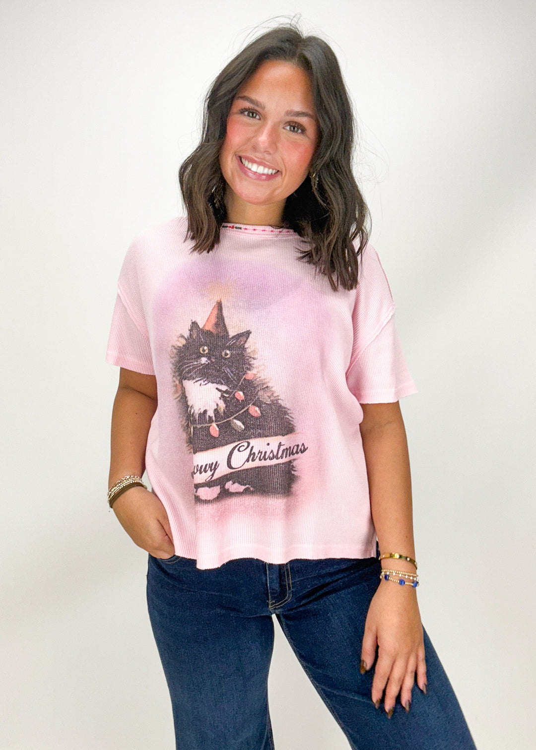Woman wearing a pink t-shirt with a cat graphic and 'Merry Christmas' text 