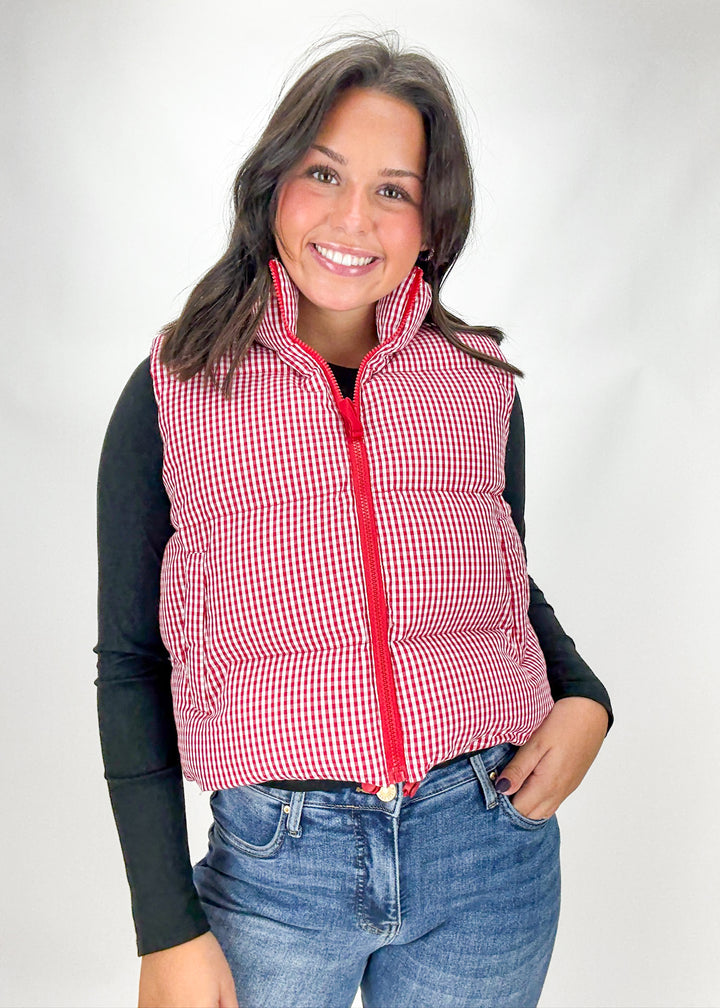 Woman wearing a red and white checkered vest over a black long-sleeve shirt and blue jeans on a white background