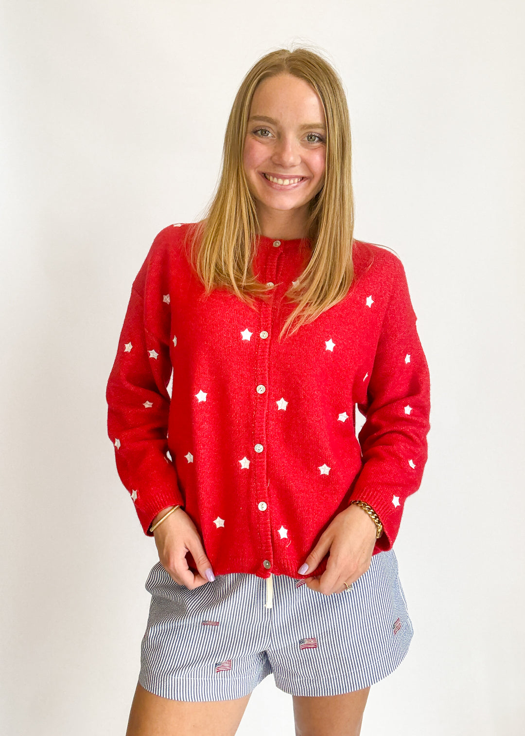 Person wearing a red cardigan with white patterns and light blue shorts on a plain background