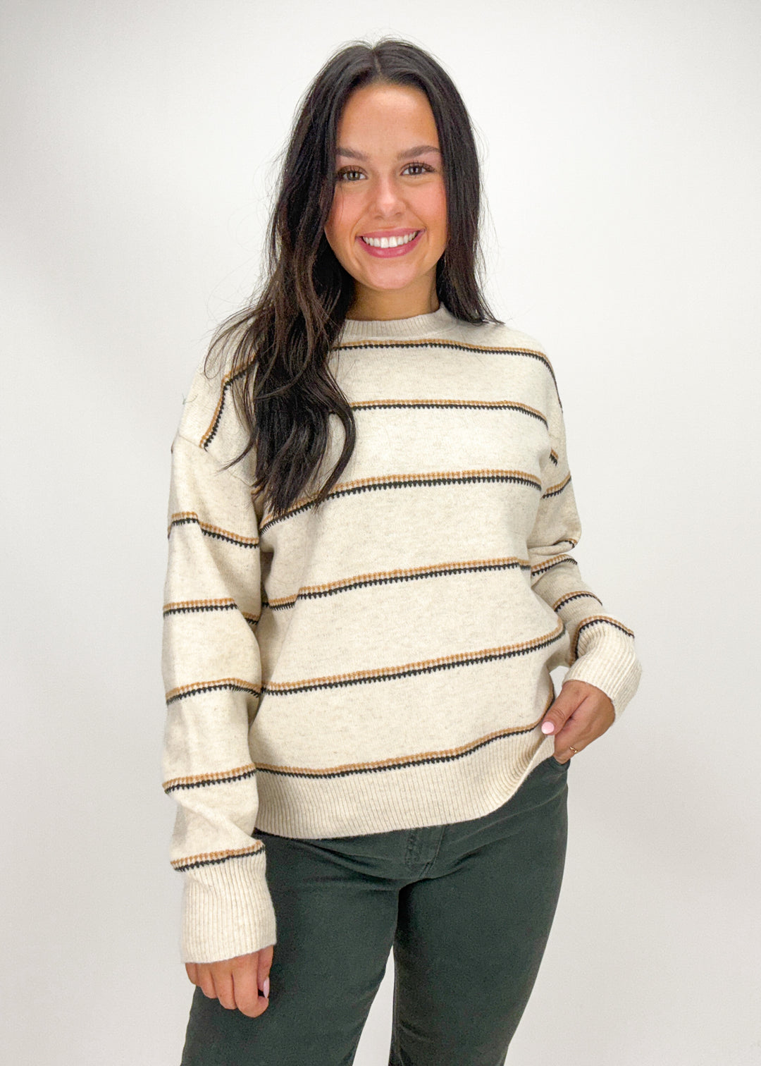 Woman wearing a cream sweater with brown stripes 