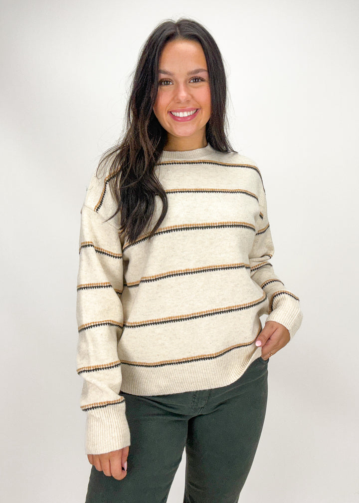 Woman wearing a cream sweater with brown stripes 