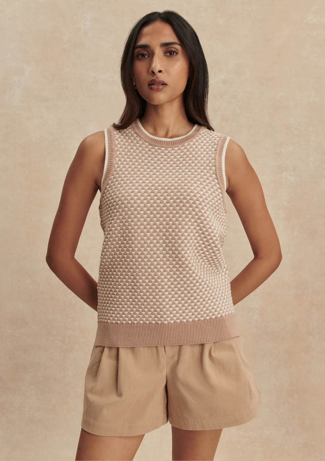 Woman wearing a beige knitted sleeveless top and shorts against a beige background