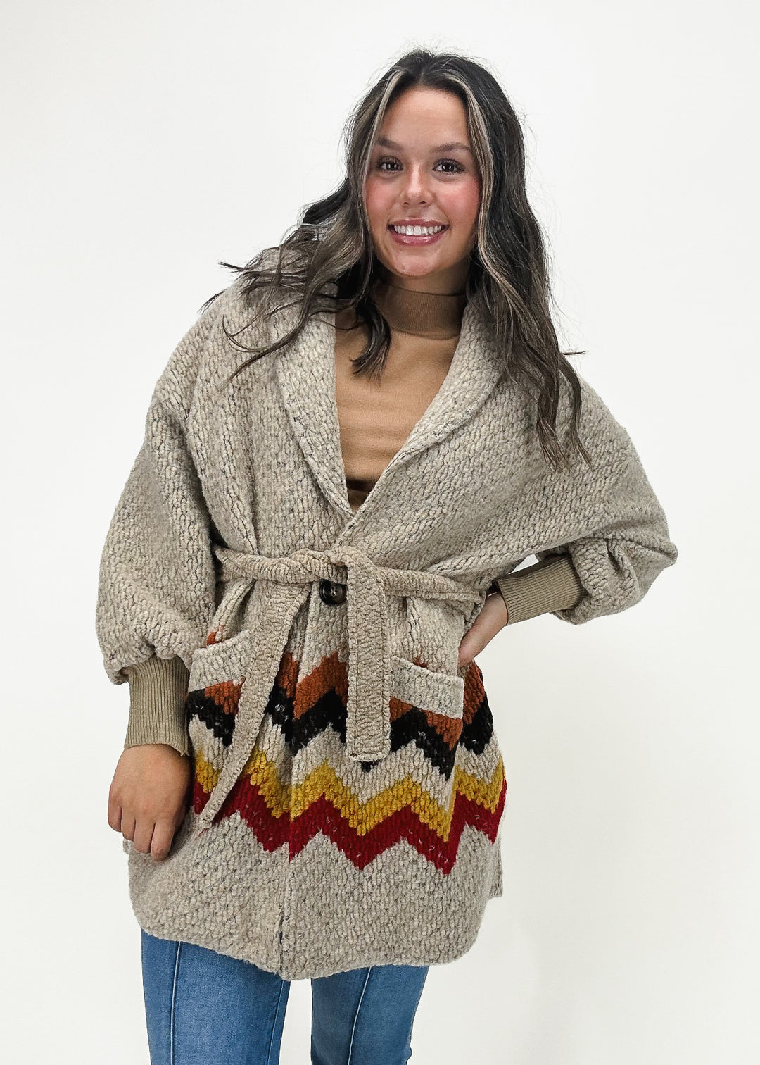 thick taupe oversized cardigan with ribbed cuff details, front pockets, a waist tie, and chevron around the waist in a mix of rust, black, gold, and red