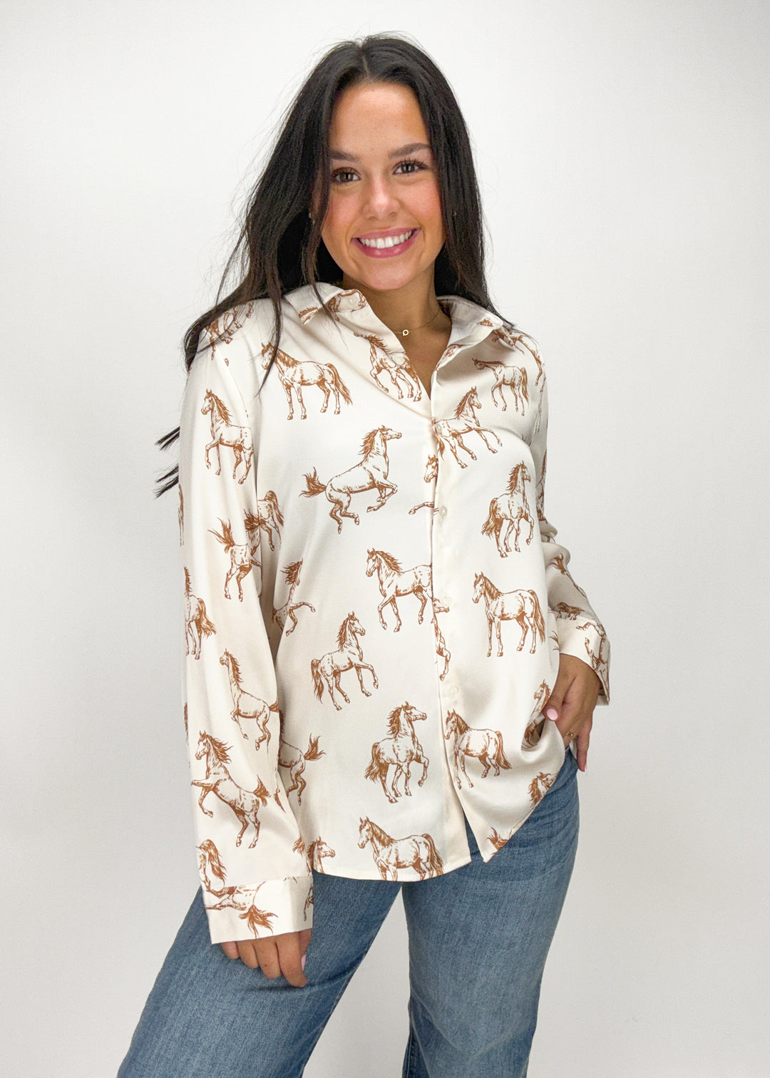 Woman wearing a cream-colored shirt with horse prints and blue jeans 
