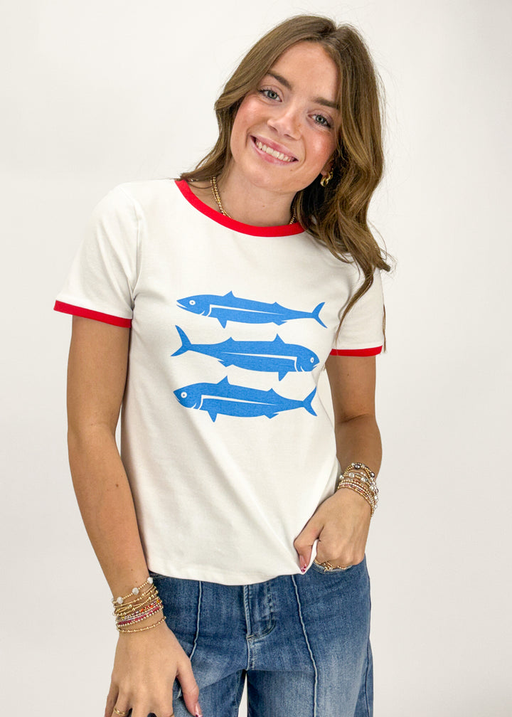 Woman wearing a white t-shirt with blue fish graphics and red trim on a plain background