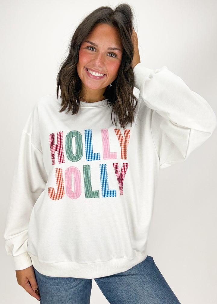 Woman wearing a white sweatshirt with 'Holly Jolly' text in colorful letters 