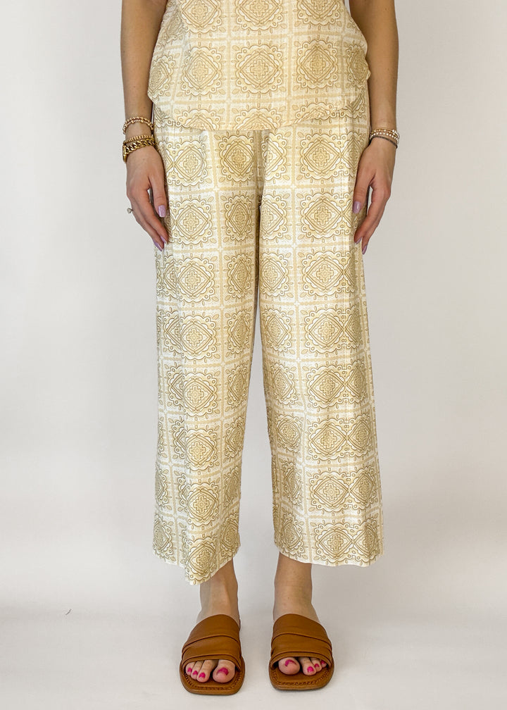 Person wearing a beige patterned outfit with wide-leg pants on a white background